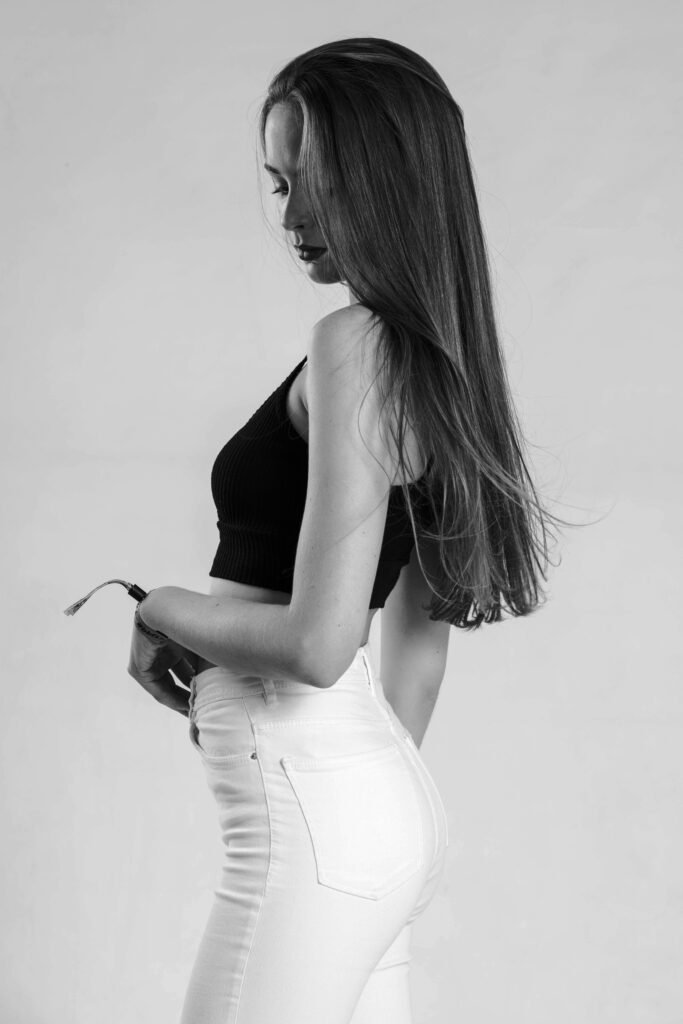 Black-and-white model test of a woman in profile with long hair, a black crop top and white jeans, against a white wall