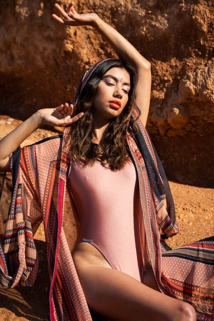 A model in a pink swimsuit and striped kimono posing against red rocks in warm sunlight