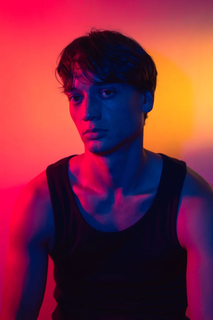 Bruin Chan in a black tank top, lit in red and orange, for the play In Other Words