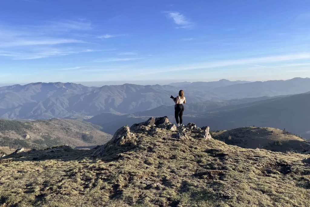 Ines Juanola standing on a rocky summit, looking out over the Pyrenees near Corsavy under a clear blue sky