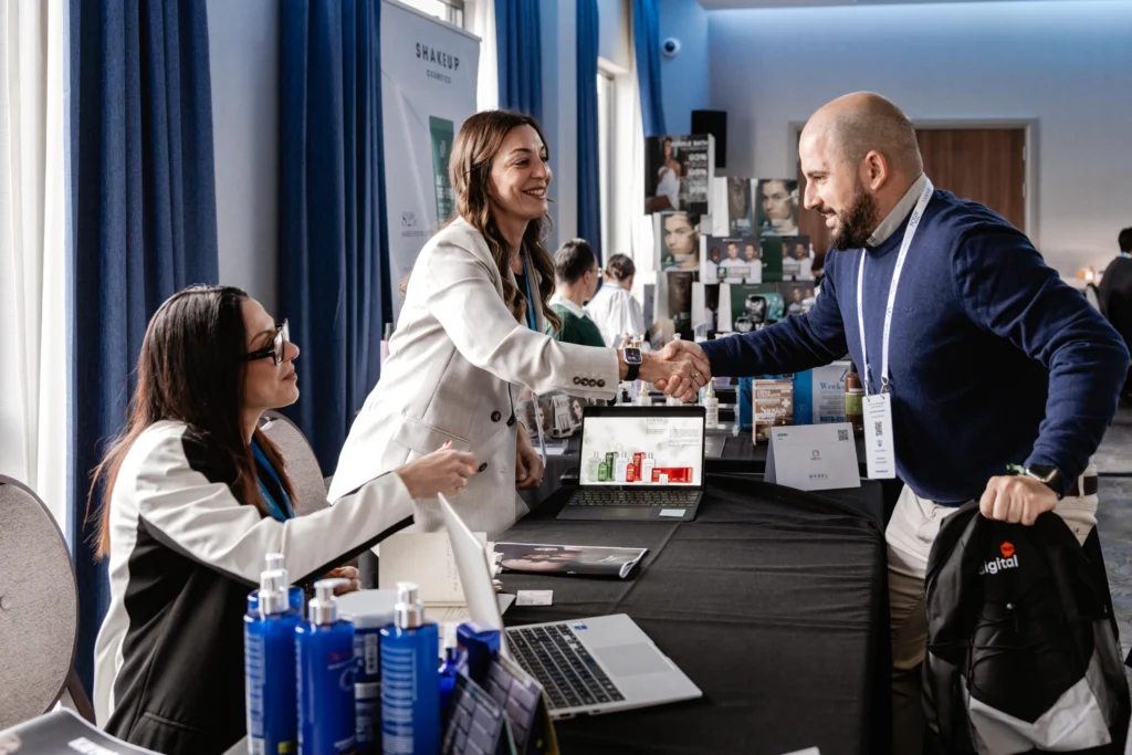 Exhibitors in white jackets greeting a visitor with a handshake at their stand during Wabel London